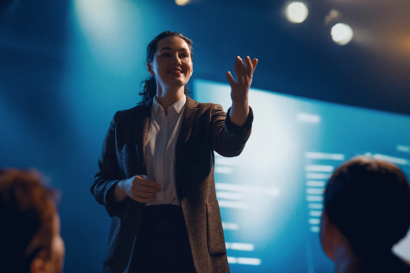 A woman presenting to an audience against a blue conference backdrop