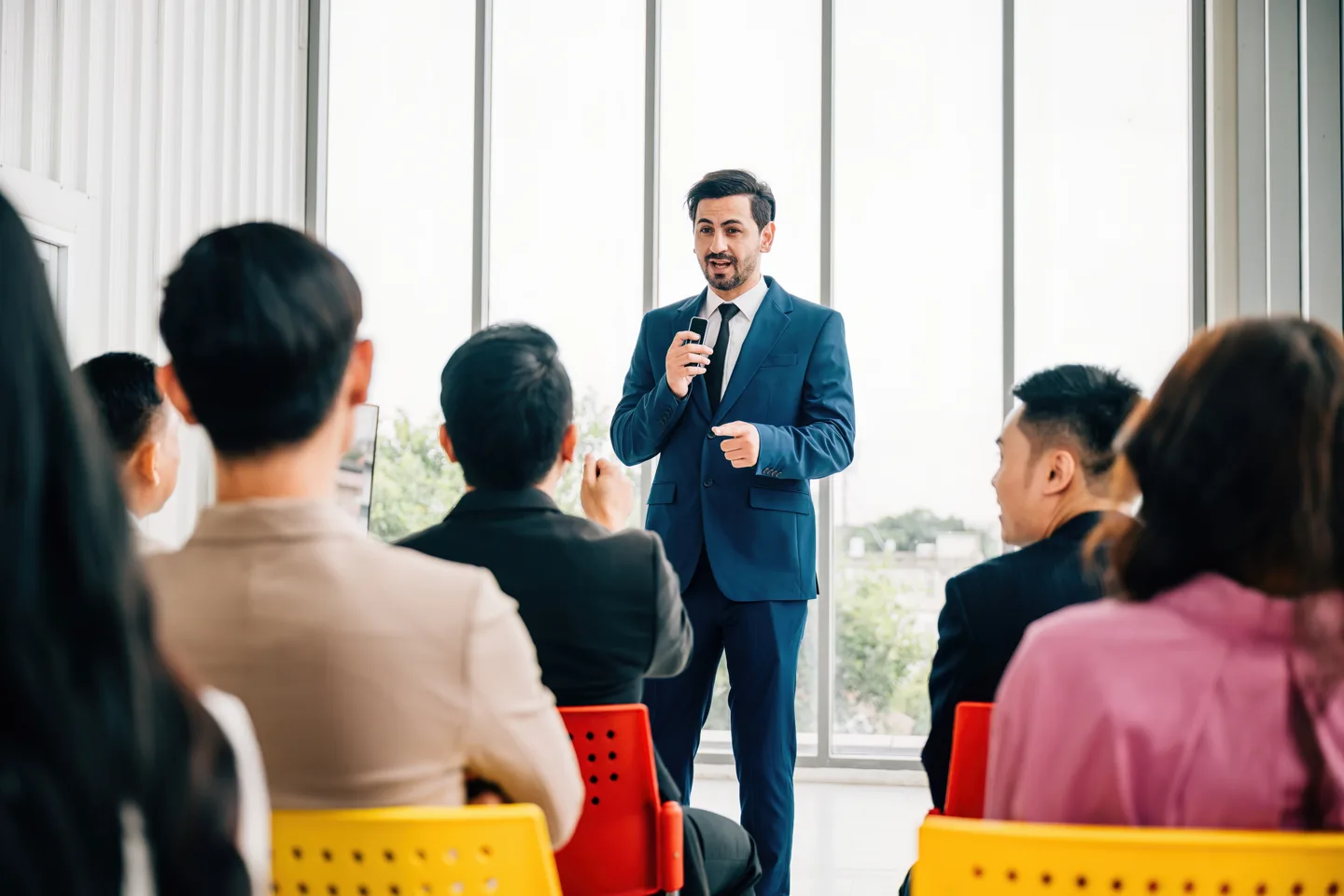 A man speaking to a seated audience in a bright business setting