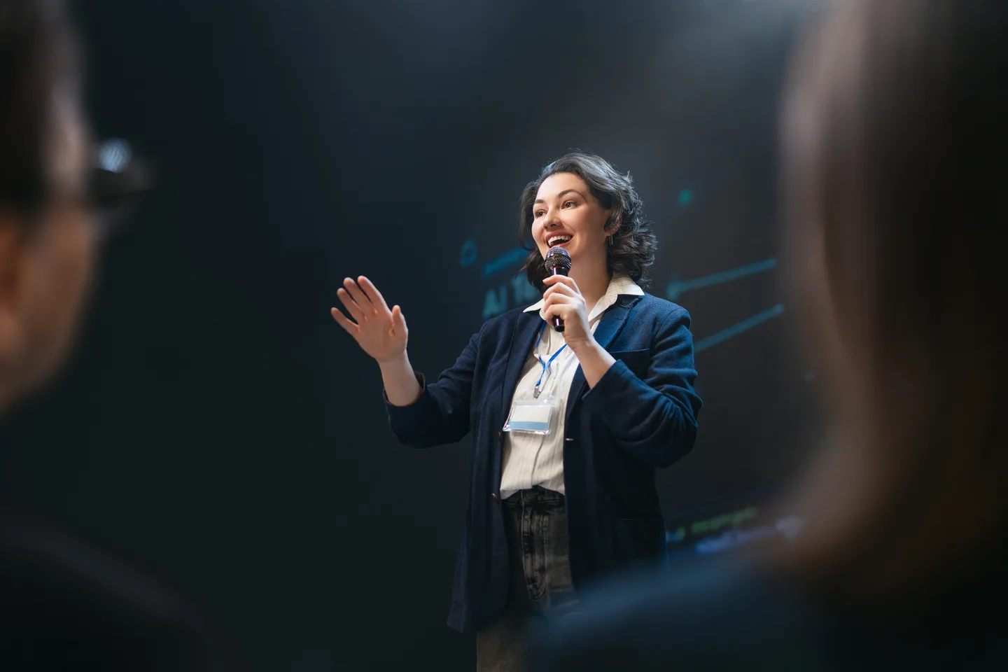 A woman delivering a presentation with a microphone on a dark stage
